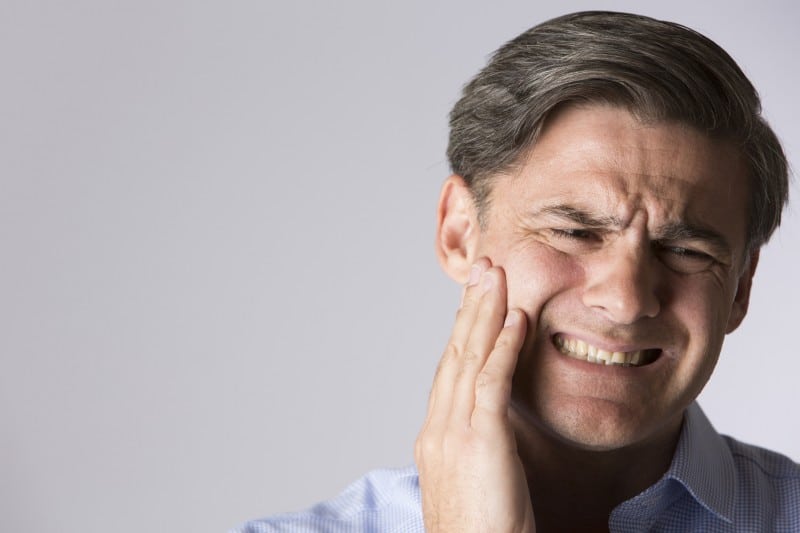 Man with jaw pain places pressure on his cheek