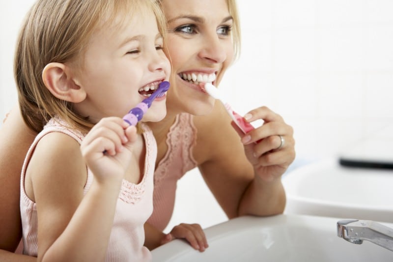 Mother and young daughter looking into the mirror while brushing their teeth