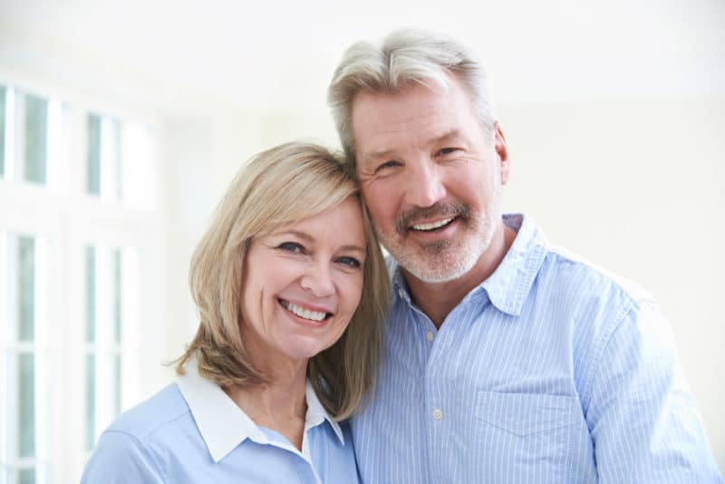 mature couple embrace while showing off their natural-looking smiles