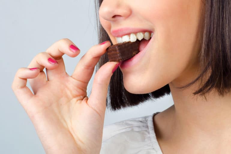Brown haired woman biting into a chocolate wafer