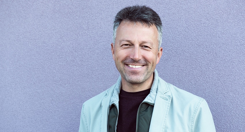 Handsome cheerful mid adult man posing over violet wall. Outdoor