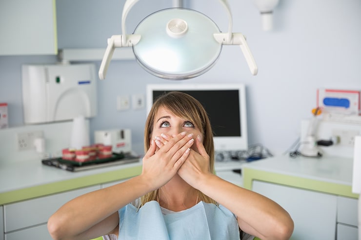 Woman sitting in her Dental clinic with hands covering her mouth, anxious for treatment