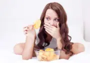 Uma mulher segurando uma batata frita enquanto tapa a boca. Ela acabou de lascar um dente?