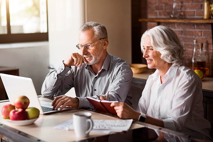 Happy Senior couple researching dental implants on a laptop while sitting in their modern kitchen