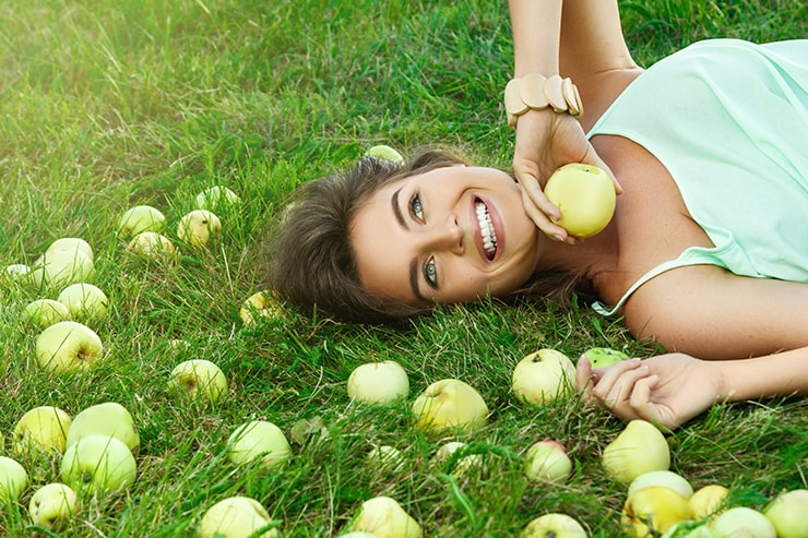 An attractive young woman laying under an apple tree. Those apples has a very destint fruity smell, just like the how you breath might smell when on the Keto diet.