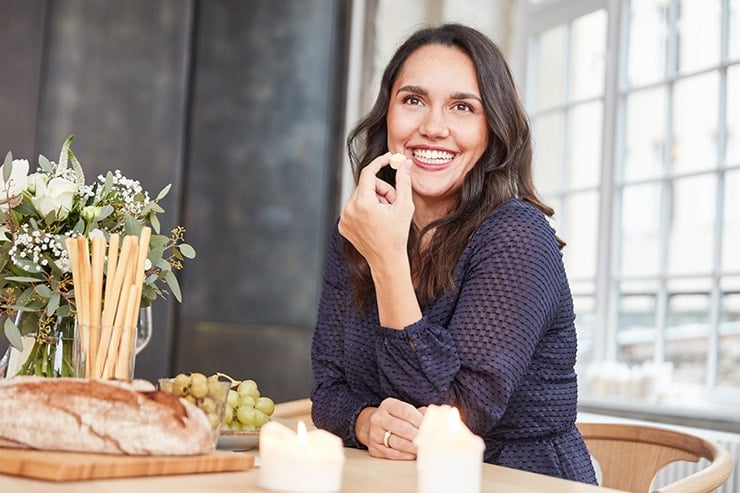 Attractive woman sitting at the kitchen table, eating and laughing. It's amazing how a dental implant has dramatically changed her smile!