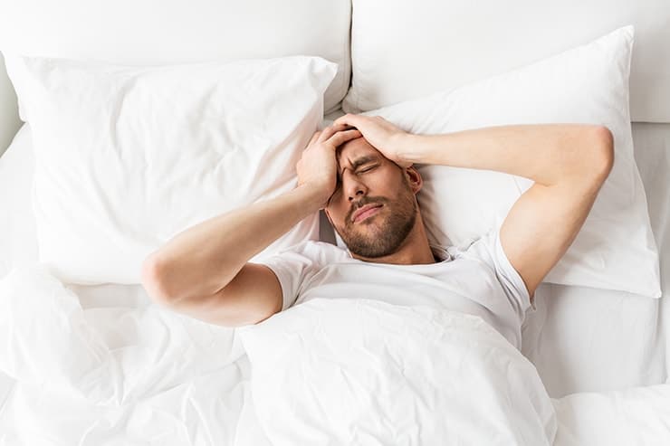 Young man waking with with a headache. For those who wake up with headaches, it can be difficult to get off on the right foot in the morning. If you tend to experience early morning headaches, there could be a few possible reasons why.