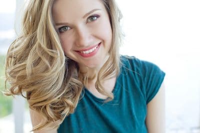 attractive young woman in blue shirt shows off healthy smile 