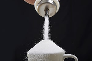 container pouring excessive amounts of sugar into a cup of coffee